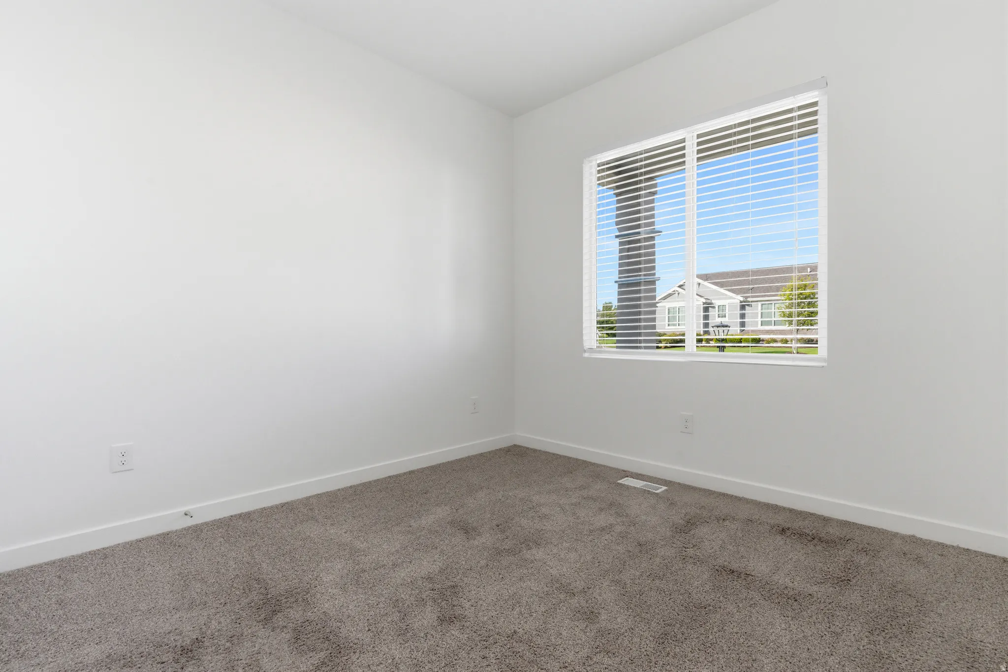 Neutral tone wall finishes with plush carpet flooring, a large window offering natural illumination, and privacy blinds