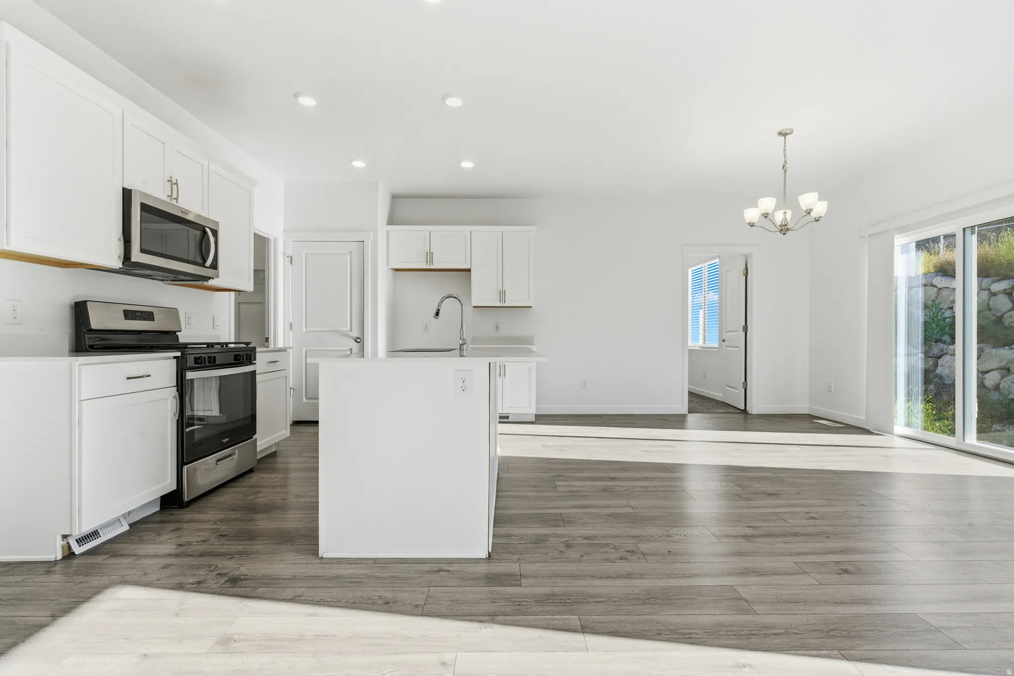 Open-concept kitchen and living area featuring wood-finish flooring, white cabinetry, stainless steel appliances, and a central island