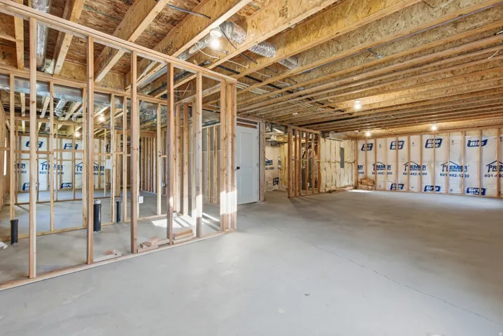 Unfinished basement space featuring visible wood framing, exposed ceiling joists, concrete flooring, rough-in plumbing, and perimeter insulation