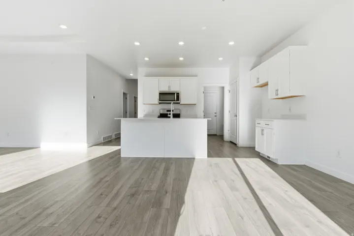 Open-concept kitchen and living area featuring wood-finish flooring, recessed lighting, white cabinetry with modern hardware, stainless steel microwave, and an integrated kitchen island