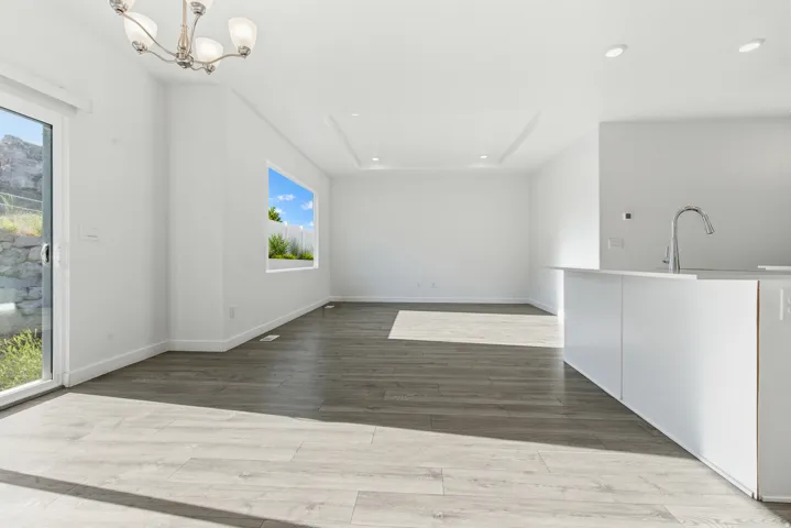 Open-concept living space featuring wood-finish flooring, a contemporary island with a gooseneck faucet, a sliding glass door, and a recessed ceiling detail