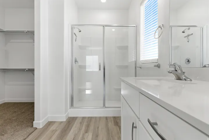Bathroom featuring a shower with sliding glass doors, a single vanity with a white countertop, and wood-finish flooring