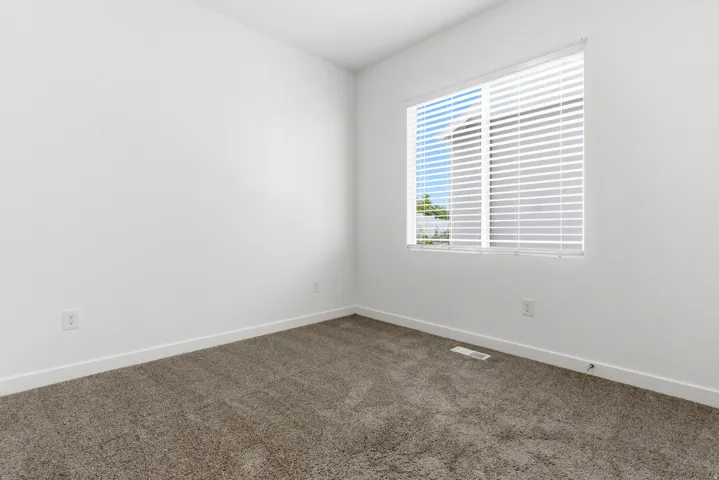 Bright room featuring a large window with horizontal blinds, plush carpeting, white baseboards, and white walls