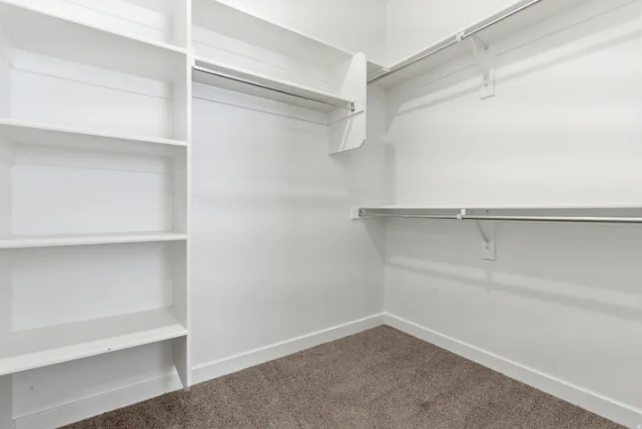 Bright, spacious closet featuring built-in shelving, two levels of hanging rods, and neutral carpet flooring