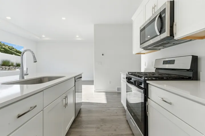 Modern kitchen featuring white cabinetry, stainless steel appliances, light countertops, a kitchen island with an undermount sink, and wood-finish flooring