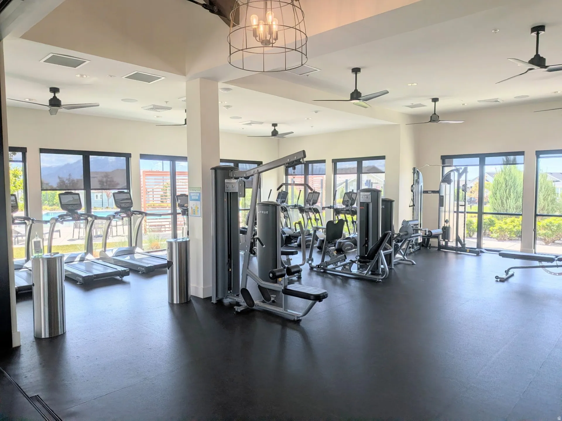 Spacious fitness center featuring high ceilings, black rubber flooring, and extensive natural light from multiple large windows