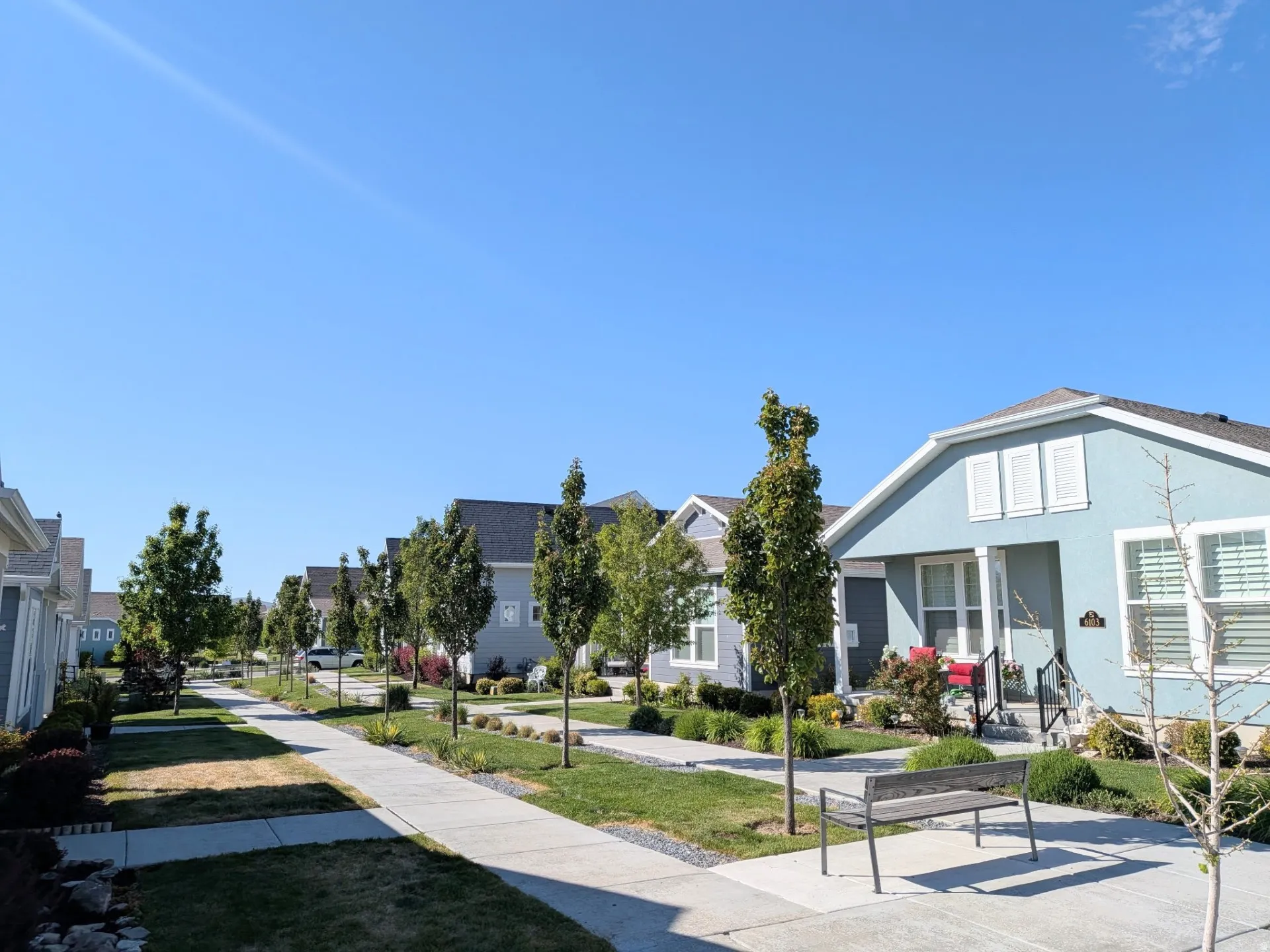 Streetscape featuring a light blue stucco home with white trim and a covered entry