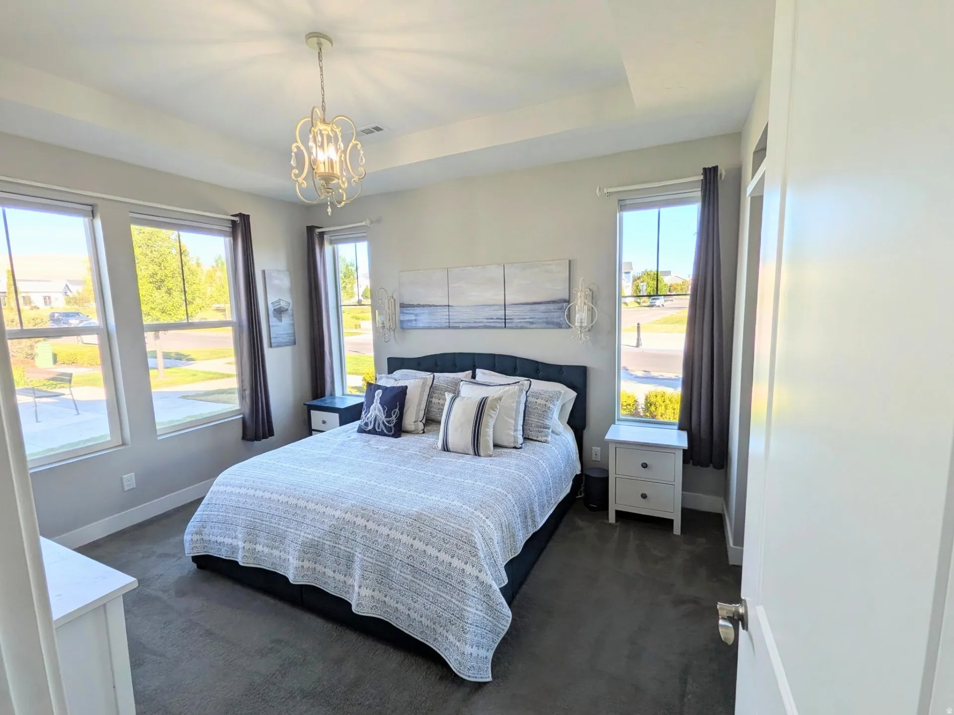 Bedroom featuring a tray ceiling with a decorative chandelier, multiple large windows, and carpeted flooring
