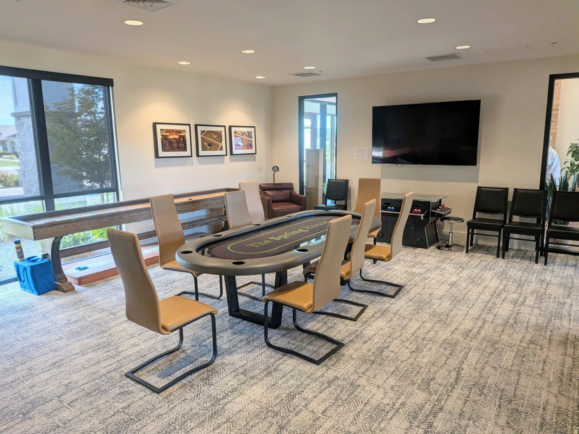 Spacious recreational area featuring a shuffleboard table, a card table with seating, and a large wall-mounted display
