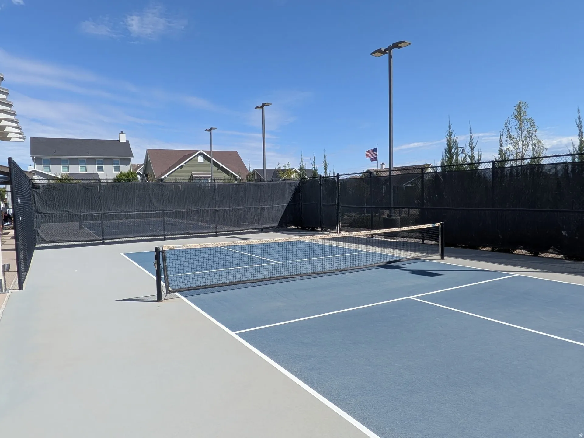 Sport court featuring a blue playing surface with white line markings, a black net, and perimeter fencing with privacy screening