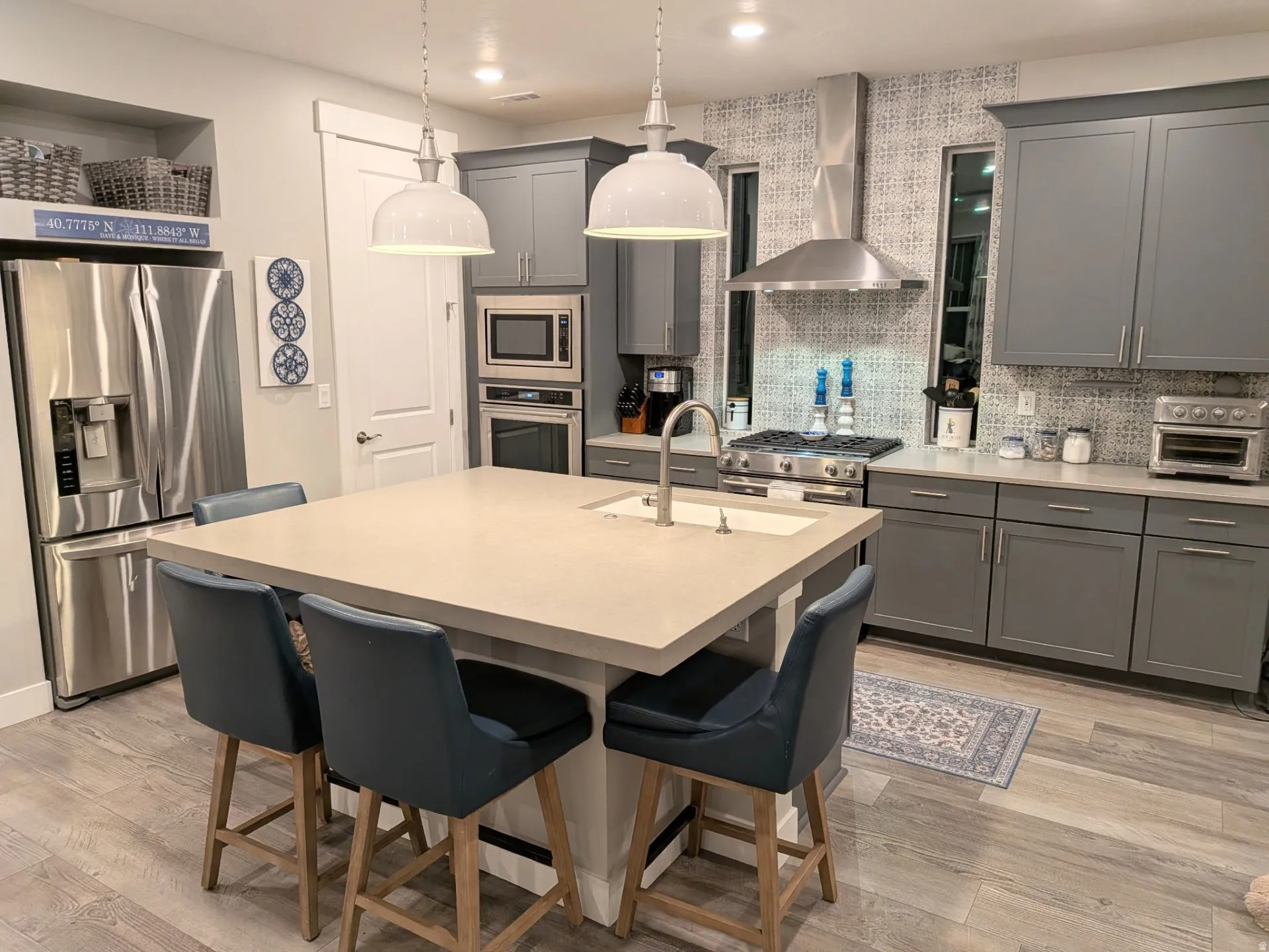Kitchen featuring a central island with an integrated sink, pendant lighting, stainless steel appliances, and gray cabinetry with coordinating countertops