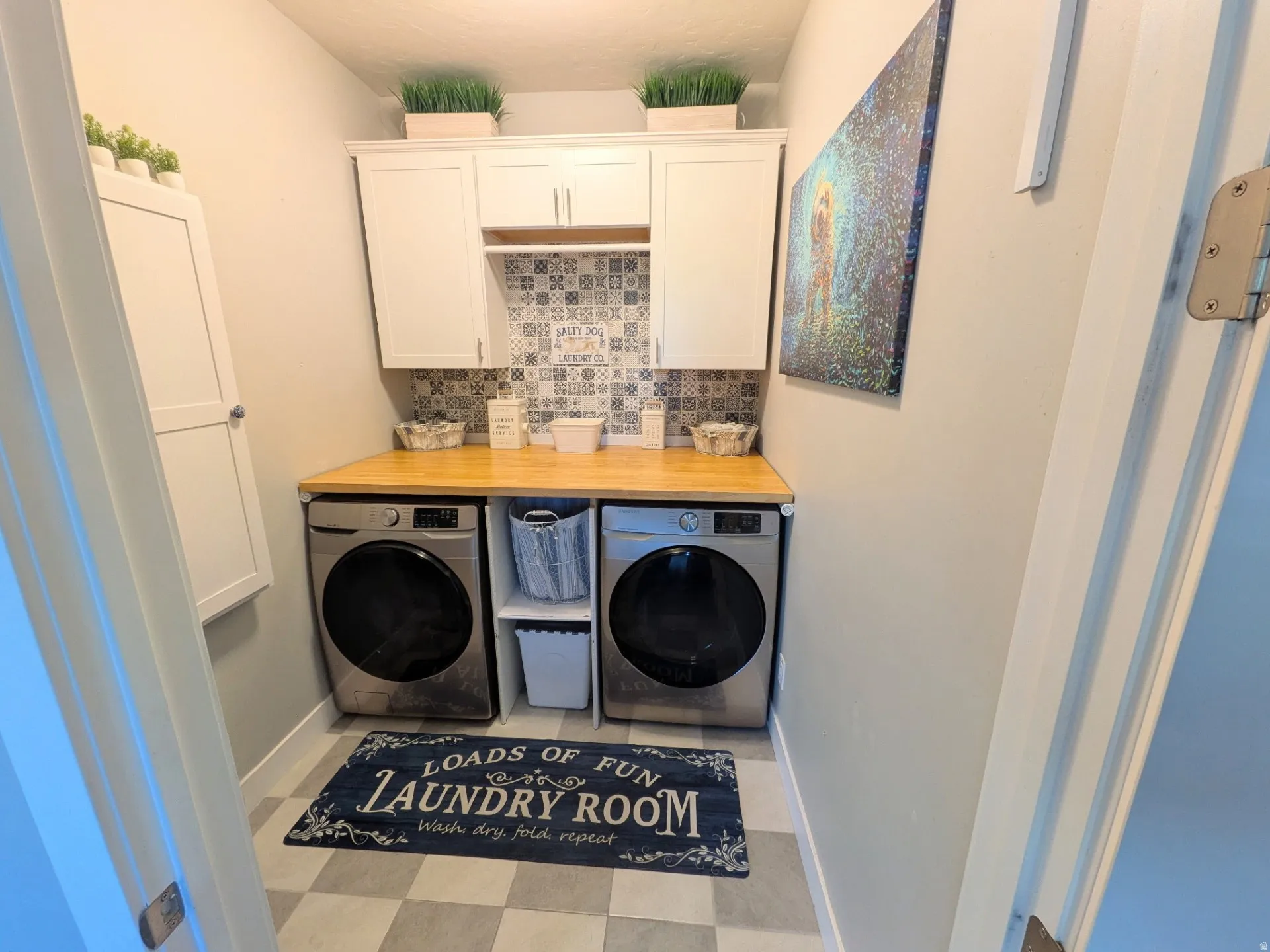 Dedicated laundry area featuring white shaker-style cabinetry and wood-finish countertops
