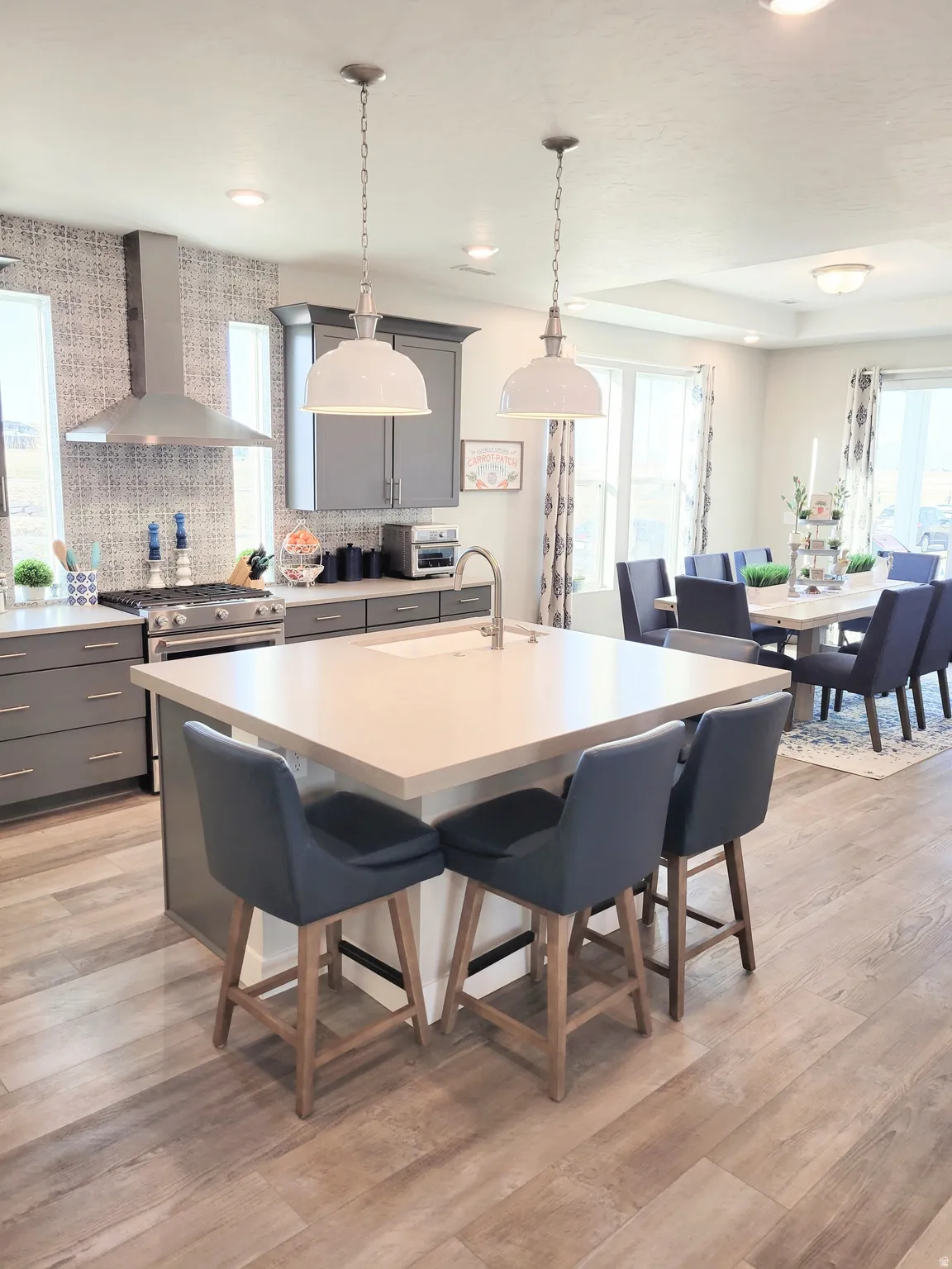 Spacious kitchen featuring an island with seating, pendant lighting, stainless steel range hood, built-in range, and wood-finish flooring