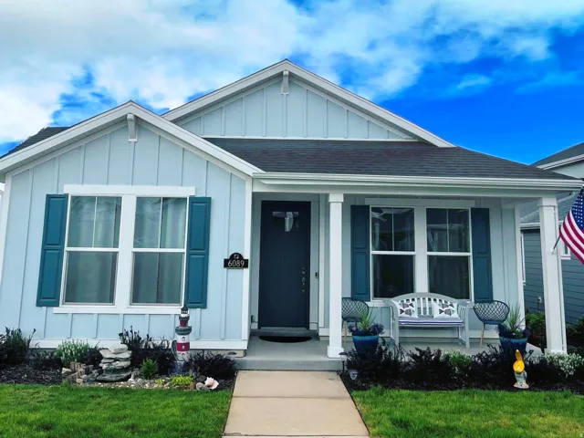 Light blue exterior with white trim, dark shutters, covered front porch, and a well-maintained lawn