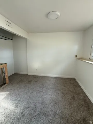 Plush carpet flooring, white painted walls, ceiling-mounted light fixture, and a window sill