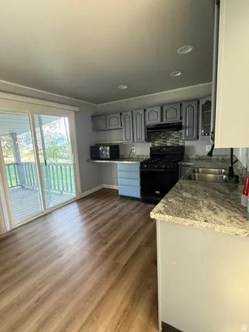 Wood-finish flooring, full kitchen with granite countertops, stainless steel sink, tile backsplash, and a sliding glass door for outdoor access