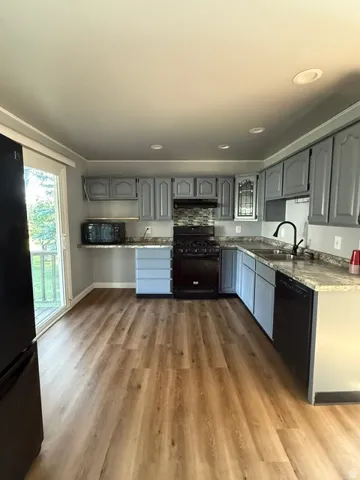 Kitchen featuring wood-finish flooring, gray cabinetry, granite-style countertops, a mosaic tile backsplash, and a sliding glass door