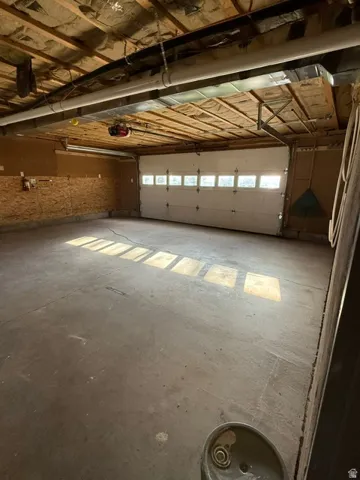 Garage with a concrete floor, a white sectional overhead door with window inserts, and visible ceiling joists