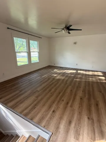 Spacious room featuring wood-finish flooring, ample natural light from multiple windows, and a ceiling fan with integrated lighting