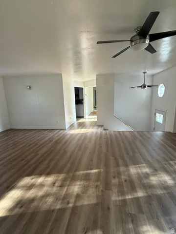 Expansive open-concept living area featuring wood-finish flooring, two modern ceiling fans, and white painted walls