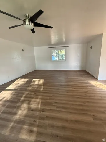Spacious room featuring wood-finish flooring, white walls, and a modern ceiling fan with integrated lighting