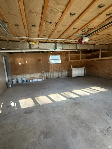 Concrete flooring, exposed ceiling joists with insulation, built-in storage shelving, and a garage door opener