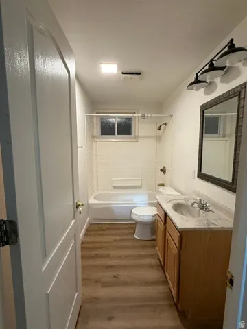 Bathroom featuring wood-finish flooring, a single vanity with a light-toned countertop, a bathtub with white subway tile surround, and a wall-mounted vanity light fixture