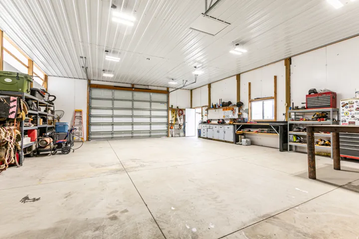 Spacious garage featuring a large roll-up door, concrete flooring, overhead lighting, and built-in workbench cabinetry