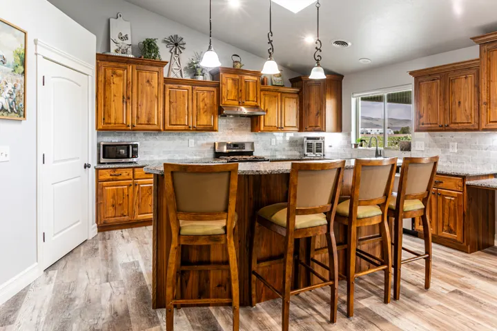 Kitchen featuring wood-finish cabinetry, a central island with countertop seating, stone countertops, a subway tile backsplash, and wood-finish flooring