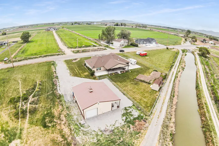 Expansive rural property featuring a large detached garage with multiple bays, a single-story residence with a covered patio, and a separate storage shed