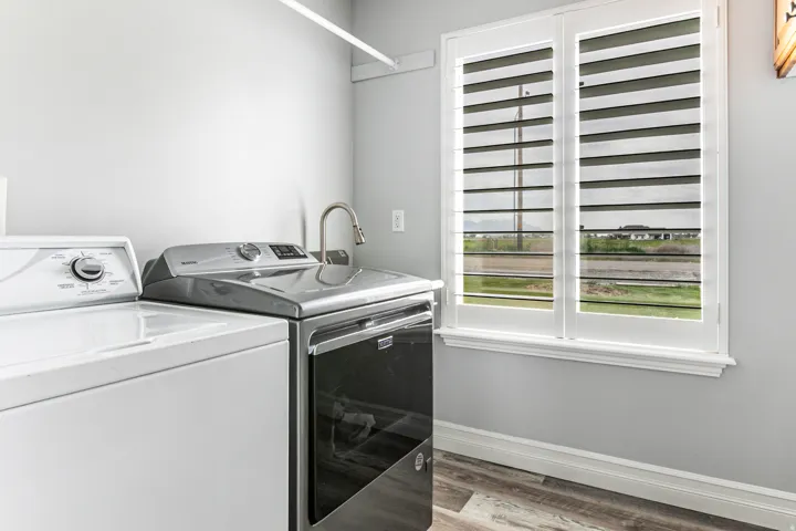 Laundry area featuring wood-finish flooring, a utility sink with a gooseneck faucet, and a double window with plantation shutters