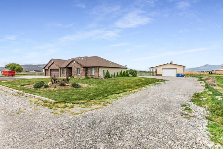 Expansive gravel driveway providing ample parking, with a large detached outbuilding featuring a roll-up door and covered patio space