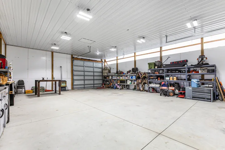 Spacious utility building featuring a concrete floor, high ceilings, exposed wood beams, multiple fluorescent lighting fixtures, and a large roll-up door