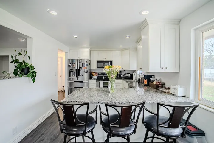 Kitchen featuring white cabinetry, light-toned granite countertops, stainless steel appliances, and dark wood-finish flooring