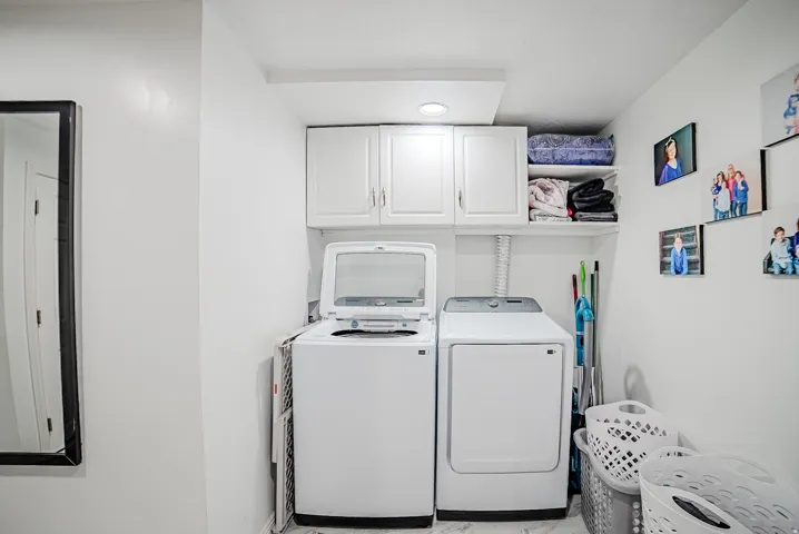 Dedicated laundry area featuring a washer and dryer, upper cabinetry, and open shelving