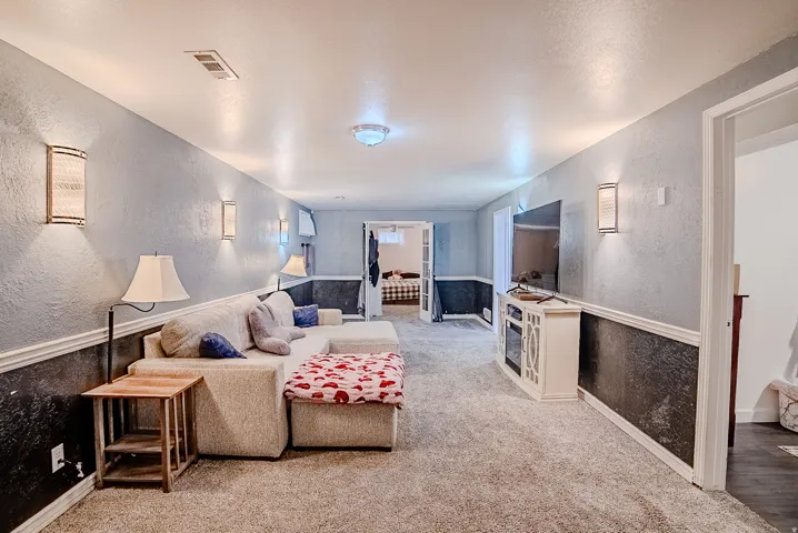 Spacious room featuring light gray textured walls with a dark gray wainscoting accent, recessed ceiling lights, and multiple wall sconces