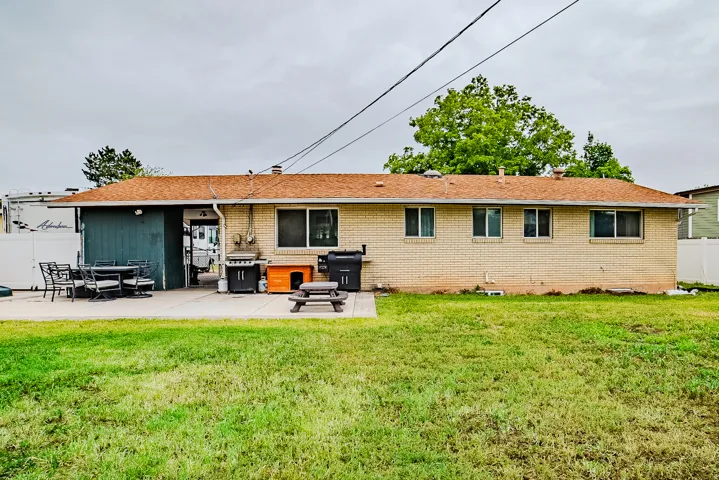 Spacious backyard featuring a large concrete patio, expansive lawn, and brick exterior with multiple windows