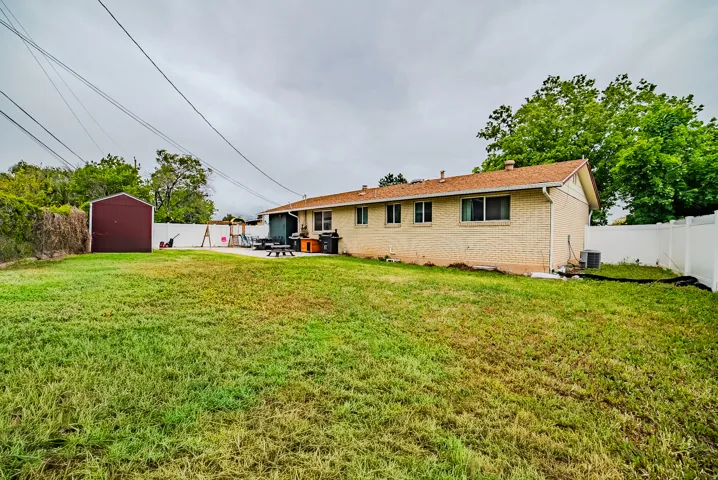 Spacious backyard featuring a large grass area, a dedicated concrete patio, and a utility shed