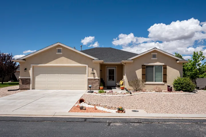 Single-story stucco exterior featuring a two-car garage, stone accents, and a low-maintenance gravel landscape
