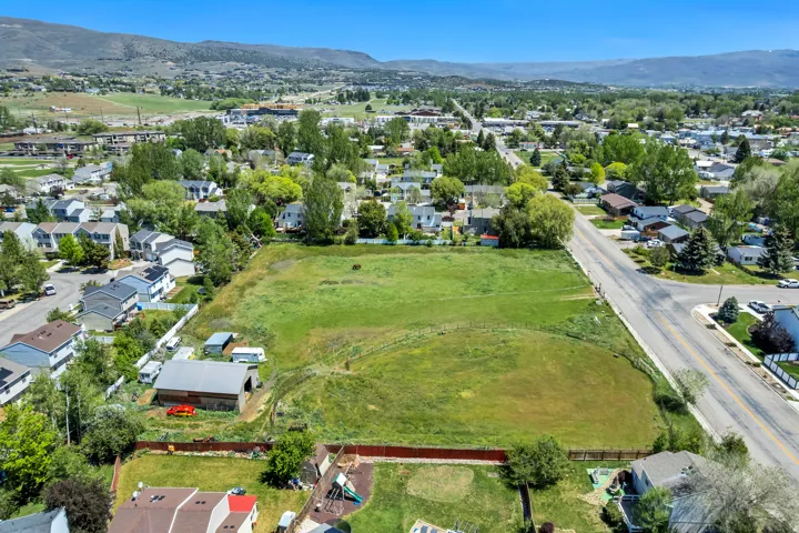 Expansive grassy parcel featuring a barn structure and surrounding mature trees, bordered by a paved road