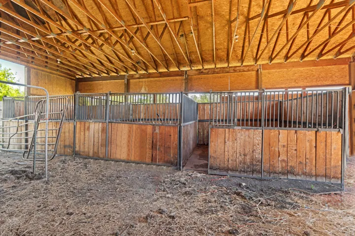 Open-air barn structure featuring multiple stalls with wood paneling and metal grating