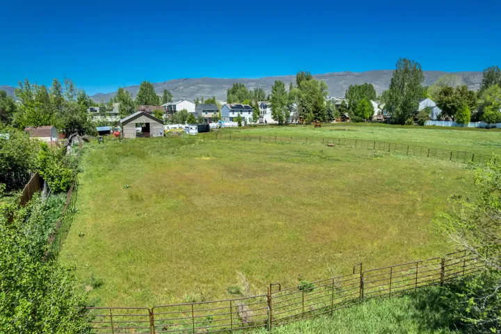 Expansive green pasture with perimeter fencing, a rustic barn structure, and distant mountain scenery