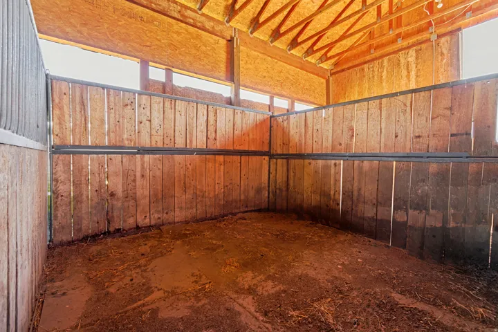 Barn interior featuring wood-paneled stalls, exposed wood ceiling beams, and upper perimeter windows