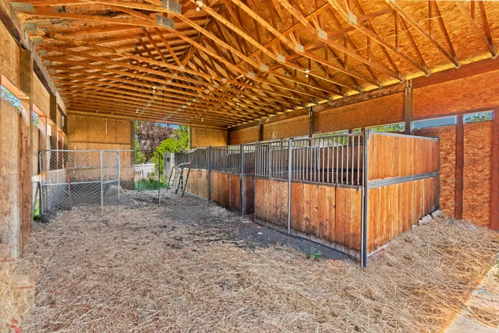 Spacious barn structure featuring a high exposed timber beam ceiling, multiple stalls with wood paneling and metal bars, and ample open floor space