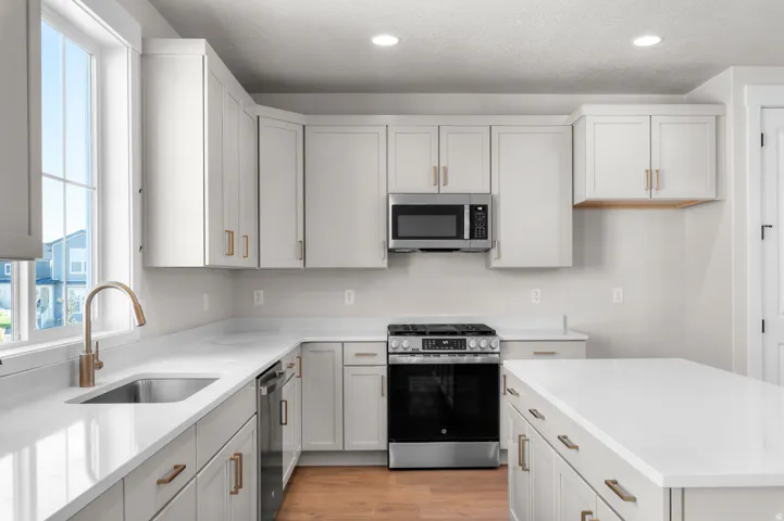 Light-toned cabinetry with brass-tone hardware, white countertops, built-in microwave, and stainless steel range