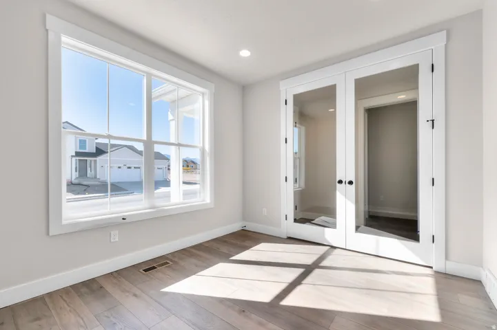 Large picture window, wood-finish flooring, recessed lighting, white trim, and glass-paned double doors