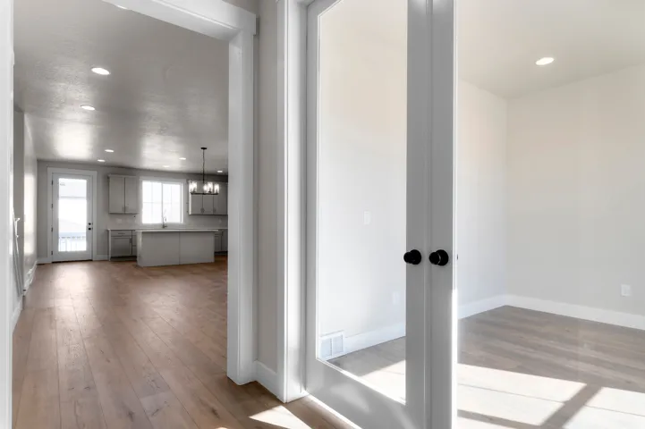 Light wood-finish flooring throughout, recessed ceiling lighting, kitchen with light cabinetry and a central island, glass-paned double doors