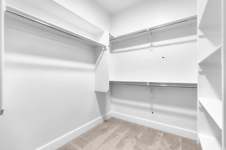 Walk-in closet featuring built-in shelving, multiple hanging rods, and carpet flooring