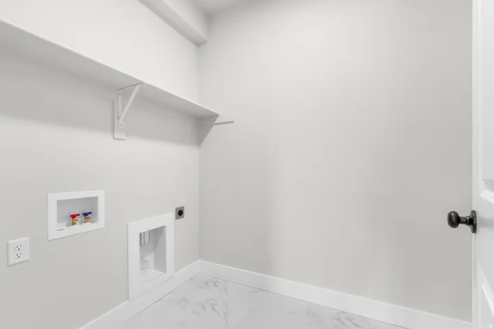 Laundry area with white shelving, white walls, and light-colored tile flooring