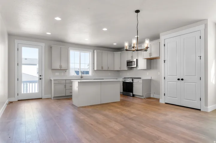 Wood-finish flooring, recessed lighting, island kitchen with light-toned cabinetry, stainless steel appliances, and a glass-paneled door
